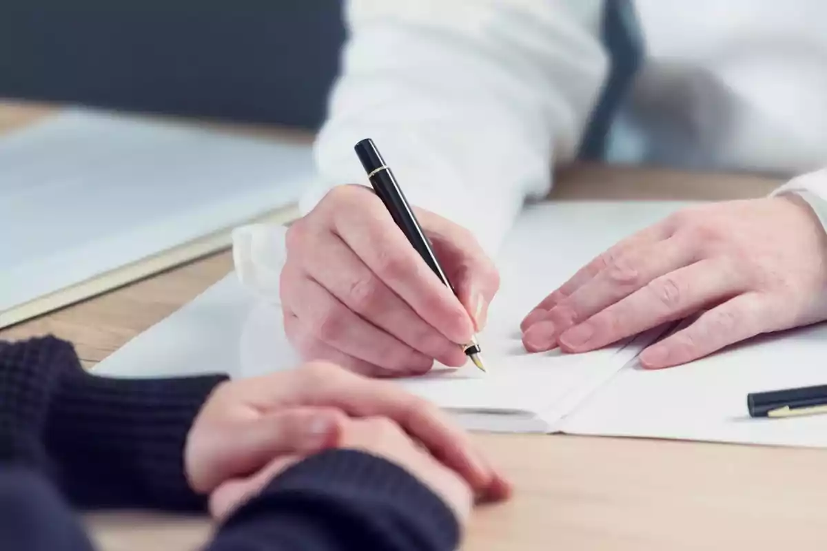 Una persona escribiendo en un documento sobre una mesa de madera.