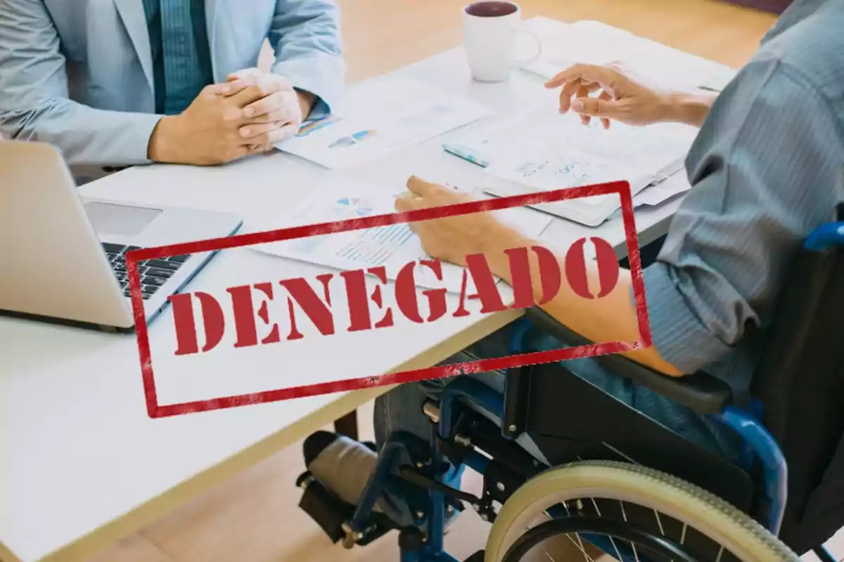 Dos personas en una reunión de trabajo con un sello de "DENEGADO" en rojo sobre la imagen.