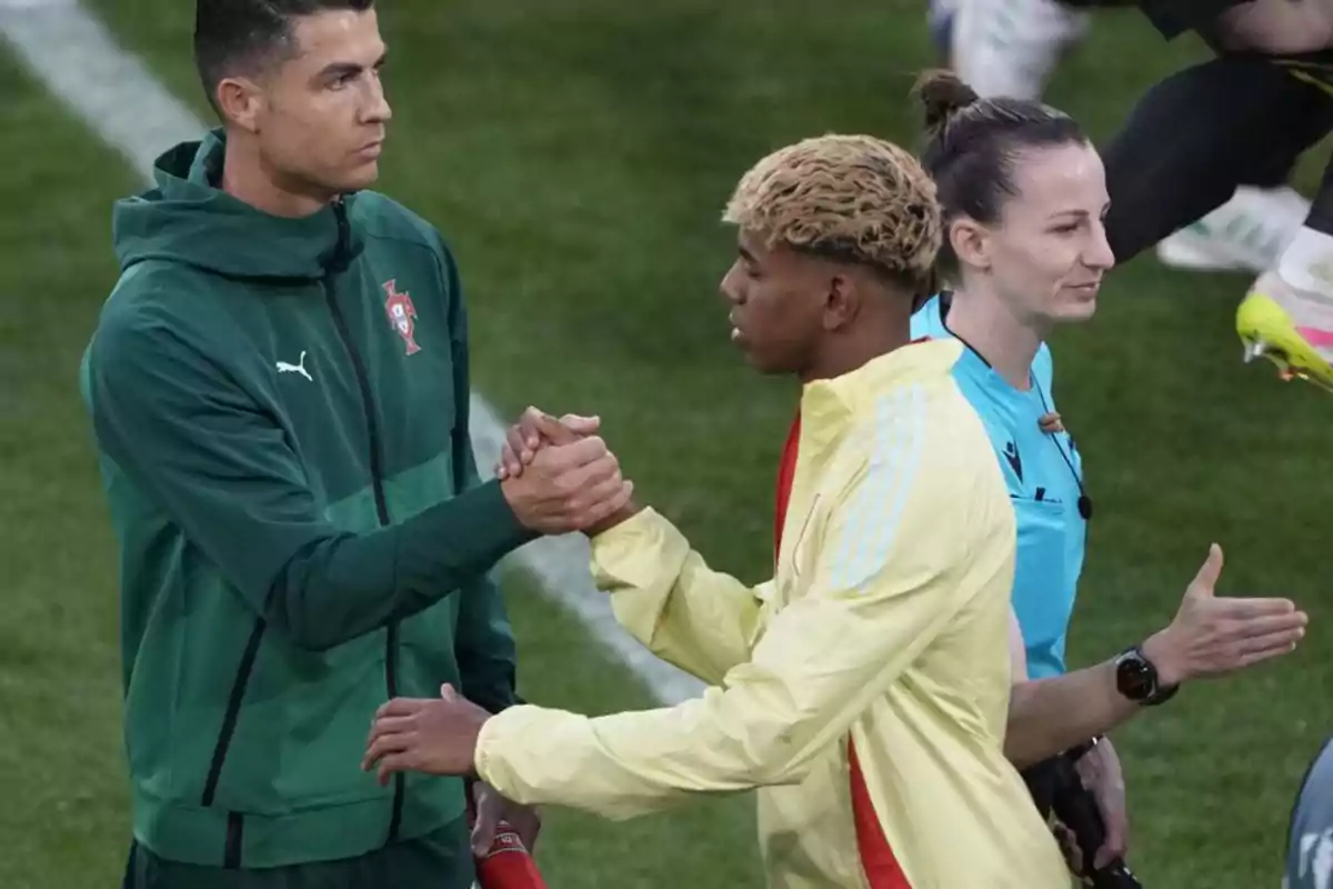 Dos futbolistas se saludan con un apretón de manos en el campo mientras una árbitra camina cerca de ellos Dos futbolistas se saludan con un apretón de manos en el campo mientras una árbitra camina cerca de ellos