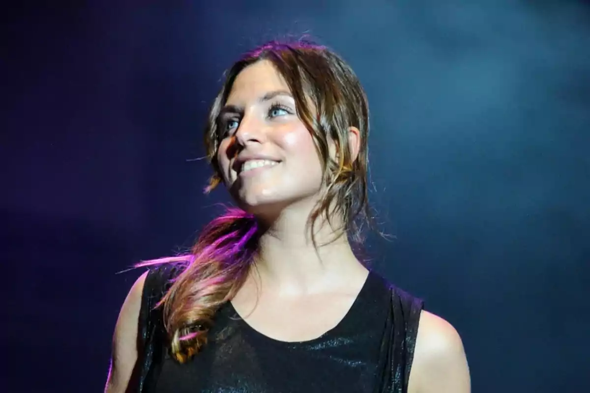 Una mujer sonriente con el cabello recogido y un fondo oscuro.