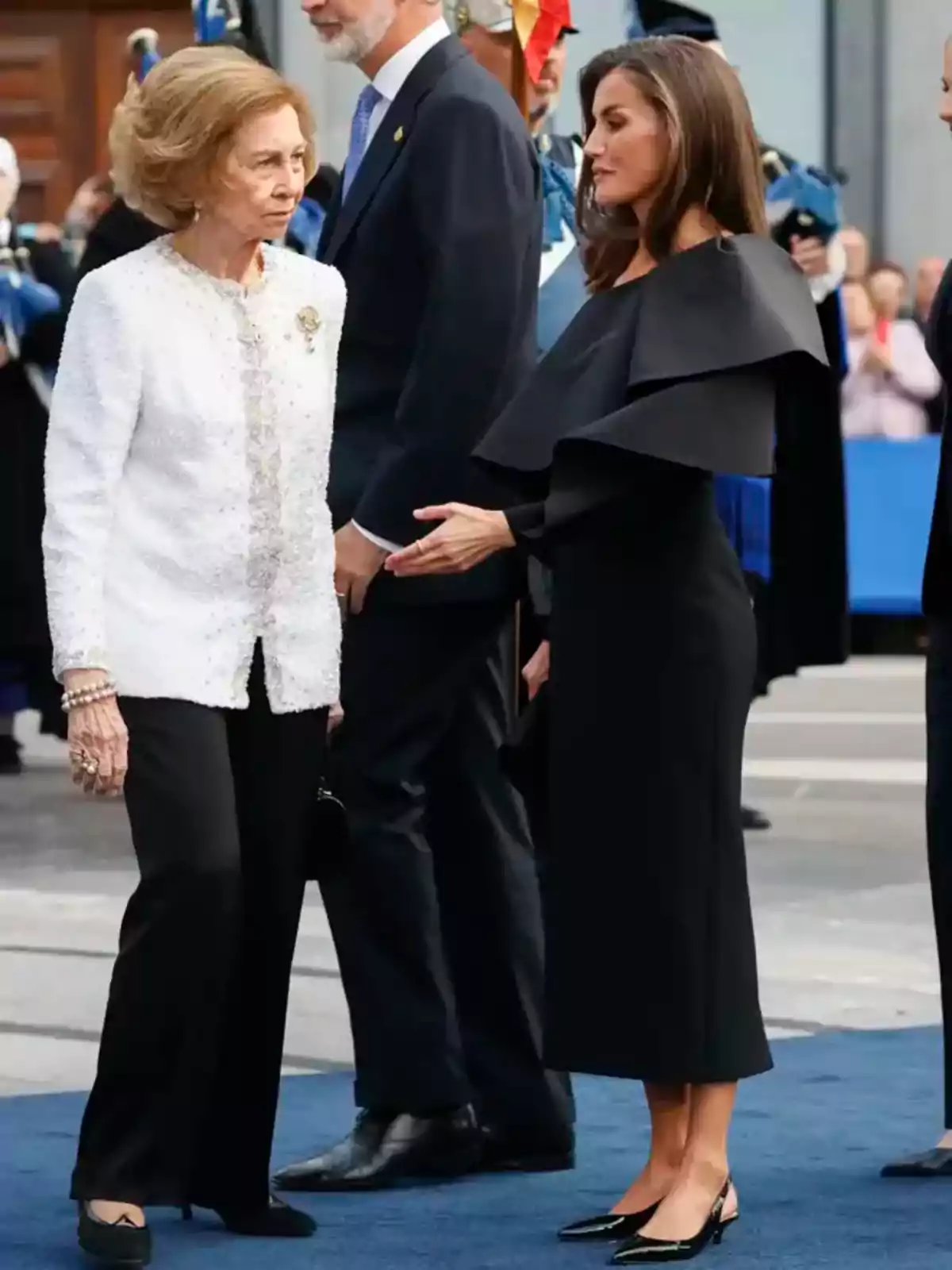 Dos mujeres elegantemente vestidas conversan en un evento formal al aire libre.