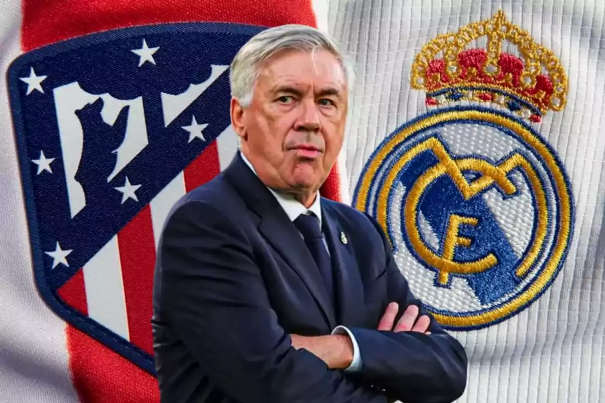 Un hombre de traje con los brazos cruzados frente a los escudos del Atlético de Madrid y el Real Madrid.