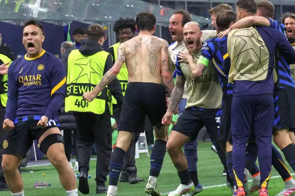 Jugadores de fútbol celebran efusivamente en el campo después de un partido, algunos con camisetas del equipo y otros sin camiseta, rodeados de personal de seguridad. Jugadores de fútbol celebran efusivamente en el campo después de un partido, algunos con camisetas del equipo y otros sin camiseta, rodeados de personal de seguridad.