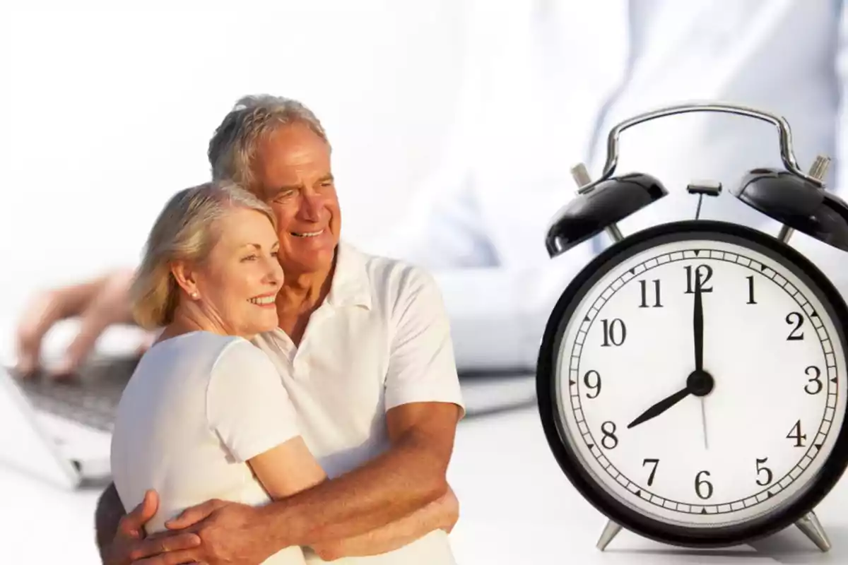 Una pareja de personas mayores abrazándose con una computadora portátil y un reloj despertador en el fondo.