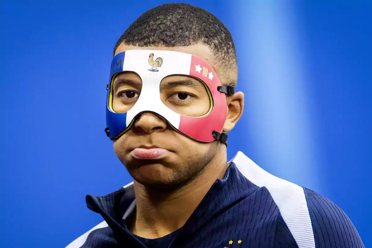 Mbappé con máscara tricolor con el escudo de Francia y el número 10, haciendo un gesto de puchero.