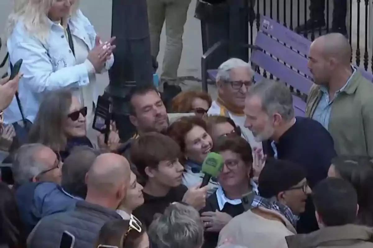 Un grupo de personas rodea a un hombre que sostiene un micrófono verde, mientras otros observan y toman fotos.