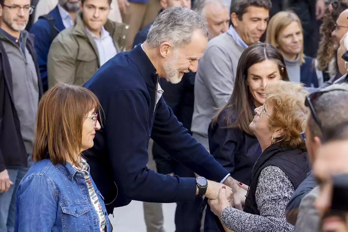 Un hombre sonriente estrecha la mano de una mujer mayor en medio de un grupo de personas.