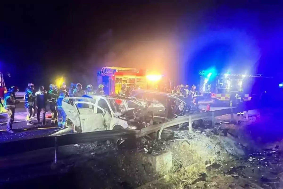 Accidente automovilístico nocturno con autos dañados y bomberos atendiendo la emergencia iluminados por luces de vehículos de rescate Accidente automovilístico nocturno con autos dañados y bomberos atendiendo la emergencia iluminados por luces de vehículos de rescate