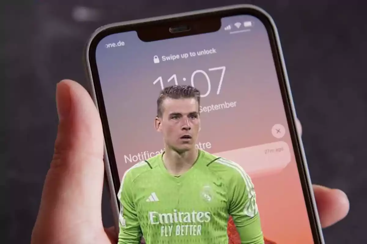 Una mano sosteniendo un teléfono móvil que muestra la pantalla de bloqueo con la imagen de un jugador de fútbol superpuesta.