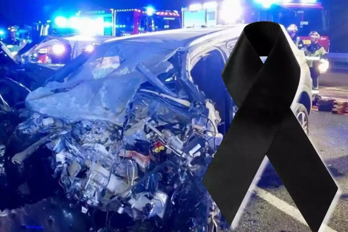 Auto destrozado tras un accidente con un moño negro de luto al frente y luces de emergencia al fondo