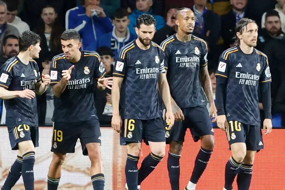 Jugadores de fútbol del Real Madrid con uniforme oscuro en el campo durante un partido.