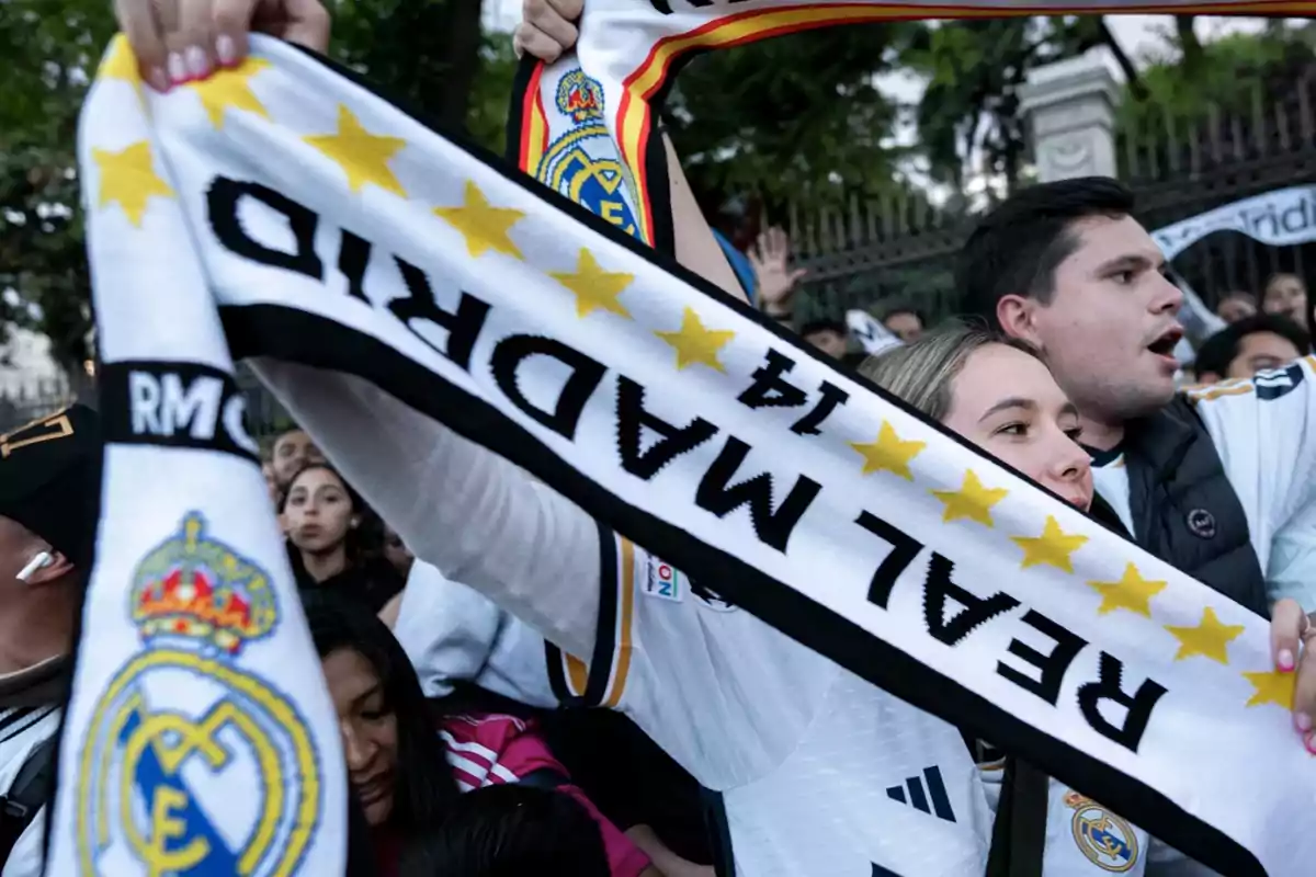 Aficionados sosteniendo una bufanda del Real Madrid con estrellas y el número 14.