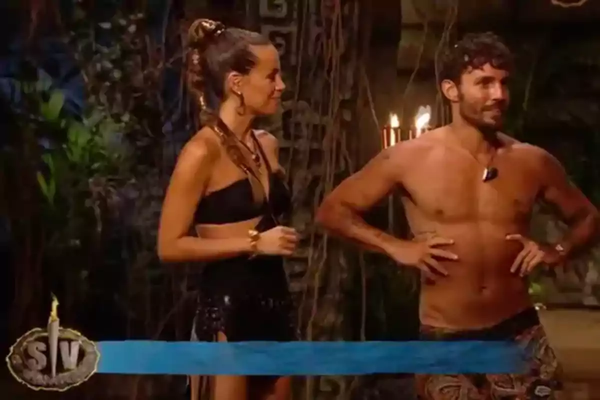 Dos personas están de pie en un entorno selvático, una mujer con un conjunto negro y un hombre sin camisa, ambos parecen estar participando en un programa de televisión. Dos personas están de pie en un entorno selvático, una mujer con un conjunto negro y un hombre sin camisa, ambos parecen estar participando en un programa de televisión.
