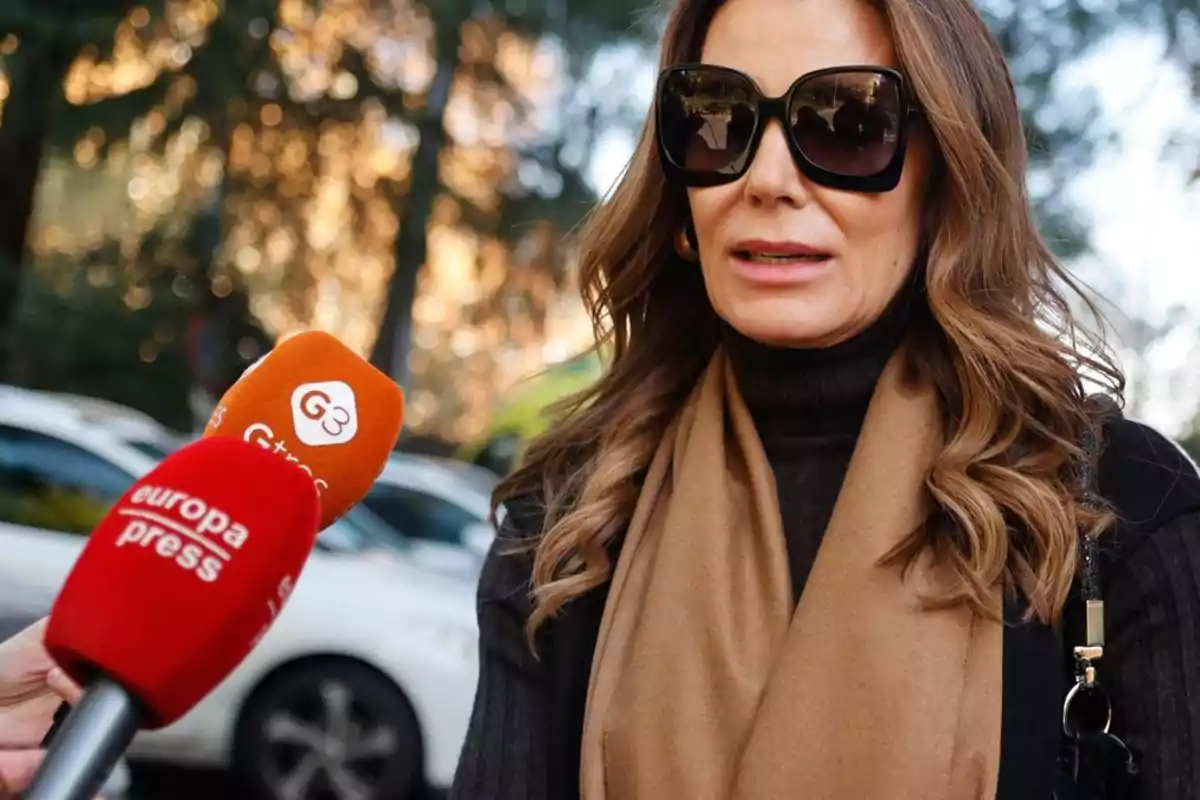 Una mujer con gafas de sol y bufanda es entrevistada por periodistas que sostienen micrófonos de Europa Press y G3.