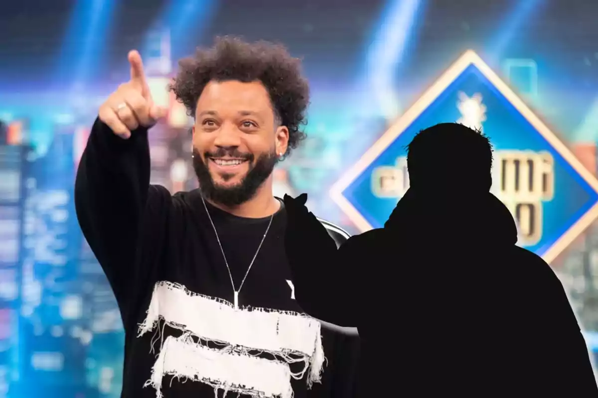 Un hombre sonriente con barba y cabello rizado señala hacia adelante, mientras una silueta oscura se encuentra en primer plano, con un fondo colorido y un letrero geométrico.