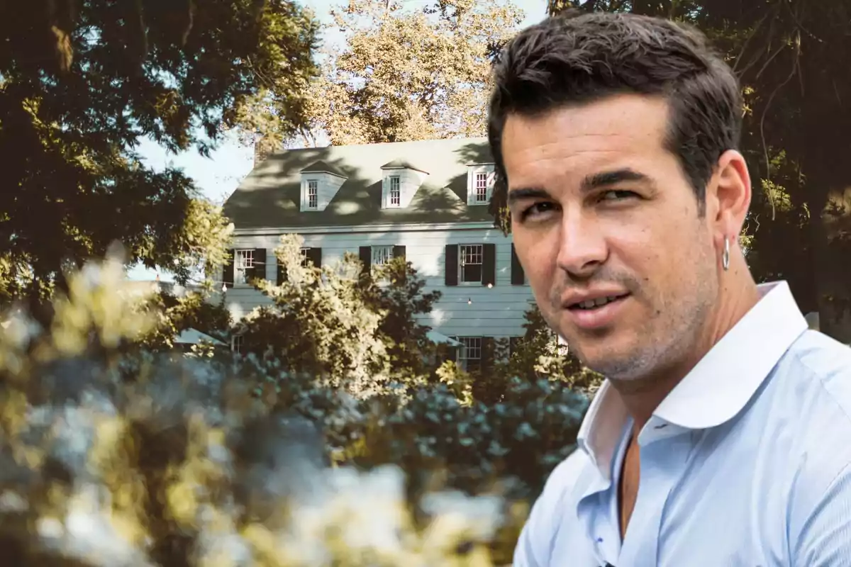 Un hombre con camisa blanca está frente a una casa de estilo colonial rodeada de árboles.