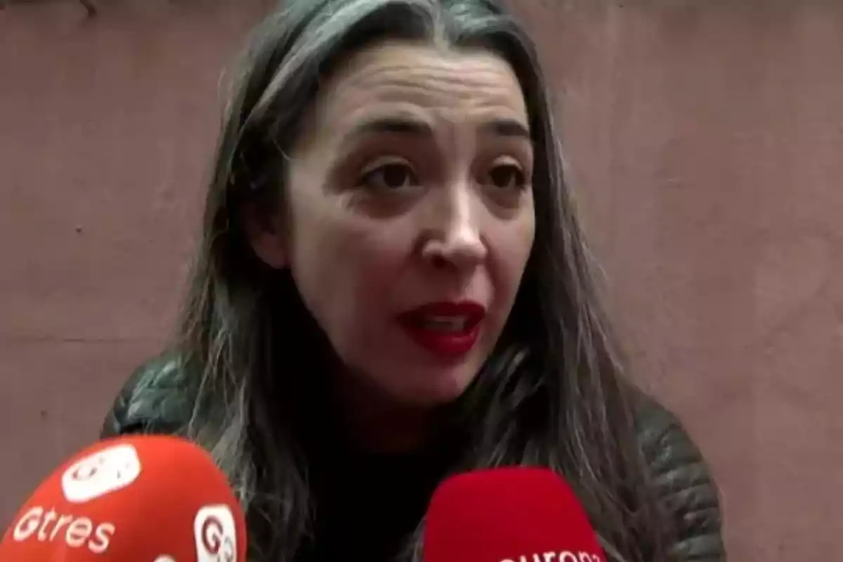 Una mujer con cabello largo y oscuro habla frente a varios micrófonos de prensa.