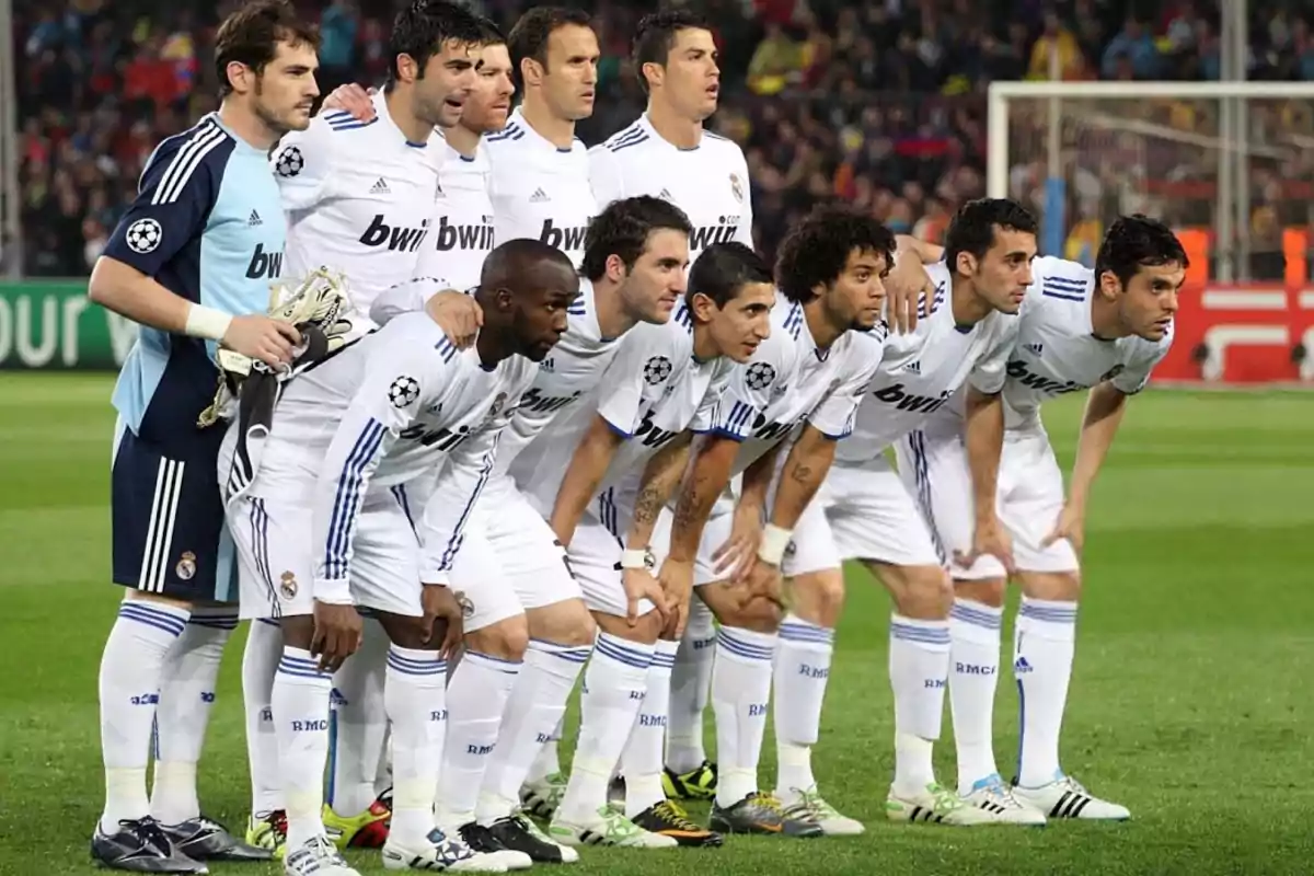 Jugadores de fútbol posando en el campo antes de un partido, todos vistiendo uniformes blancos con el logo de la UEFA Champions League en la manga.