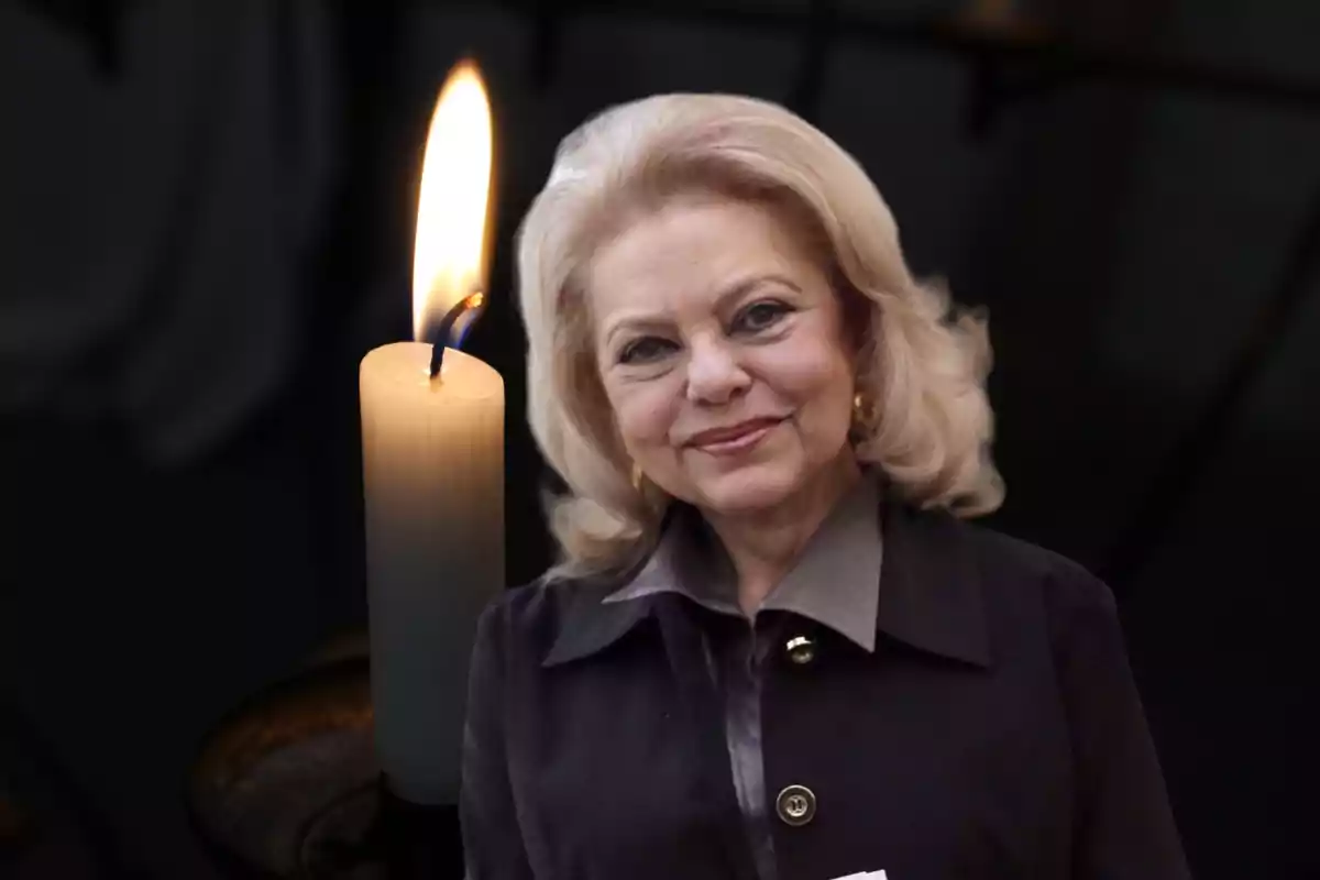 Una mujer mayor sonriente con cabello rubio y una vela encendida al fondo.