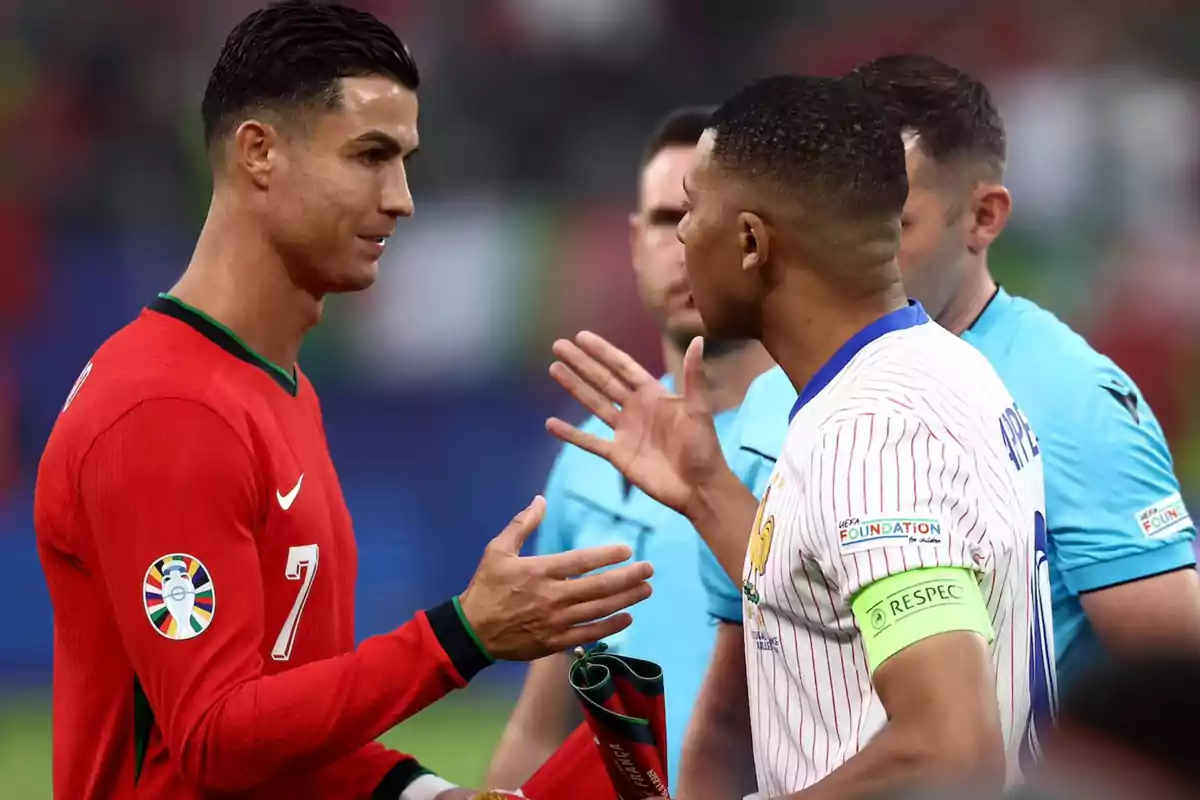 Dos jugadores de fútbol se saludan antes de un partido, uno con uniforme rojo y el otro con uniforme blanco con rayas.