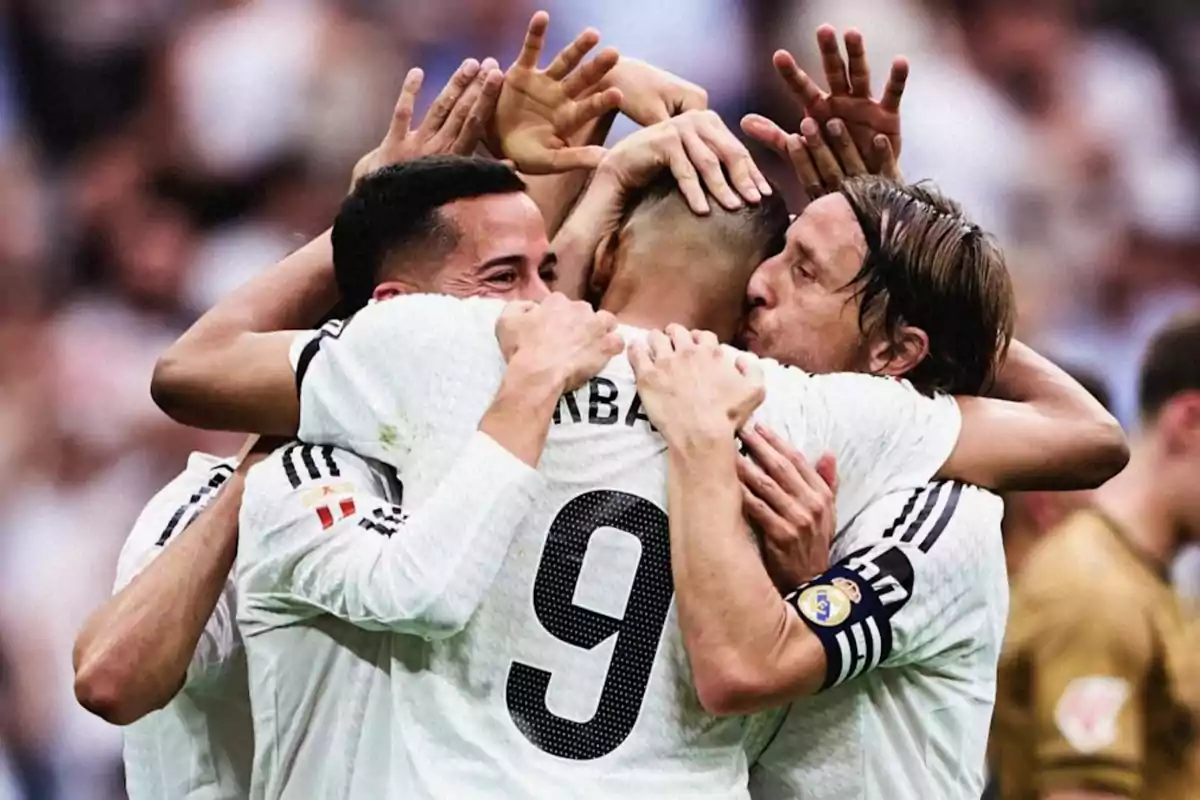 Jugadores de fútbol celebrando un gol con un abrazo en equipo en el campo.