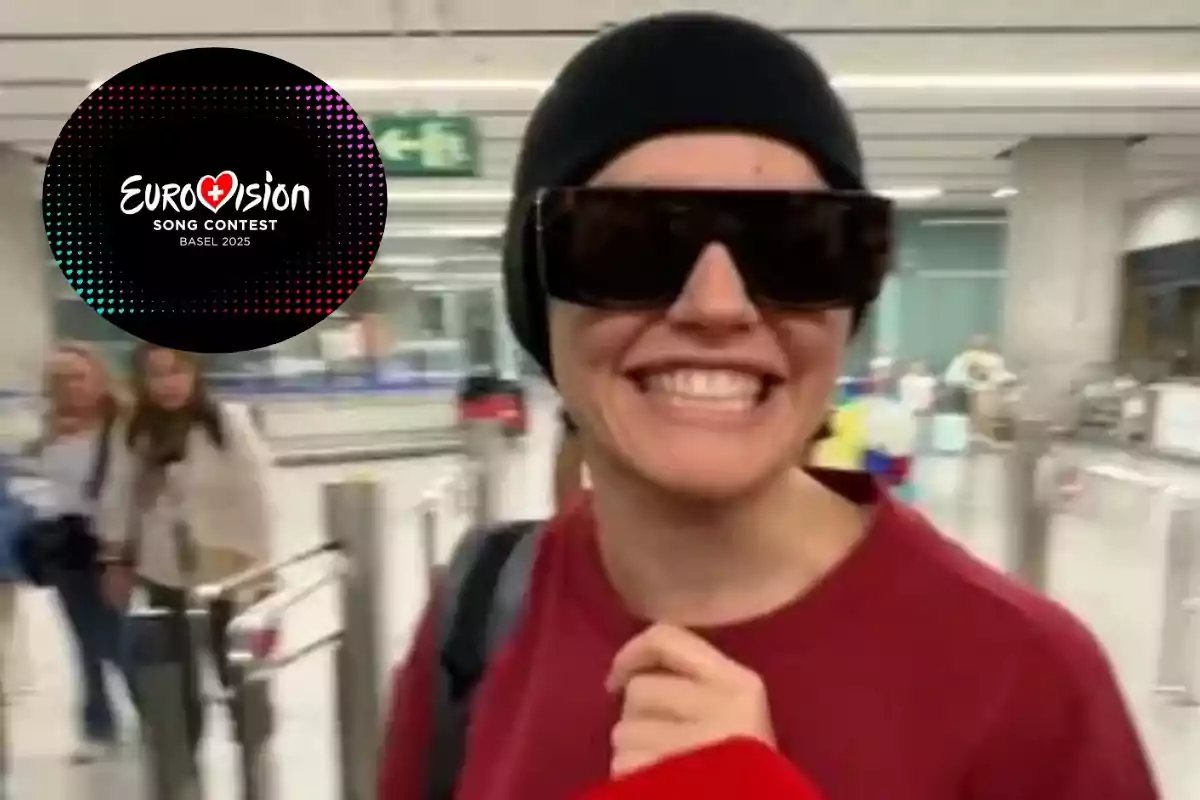 Una persona sonriente con gafas de sol y gorro negro en un aeropuerto, con un logotipo del Festival de la Canción de Eurovisión 2025 en la esquina.