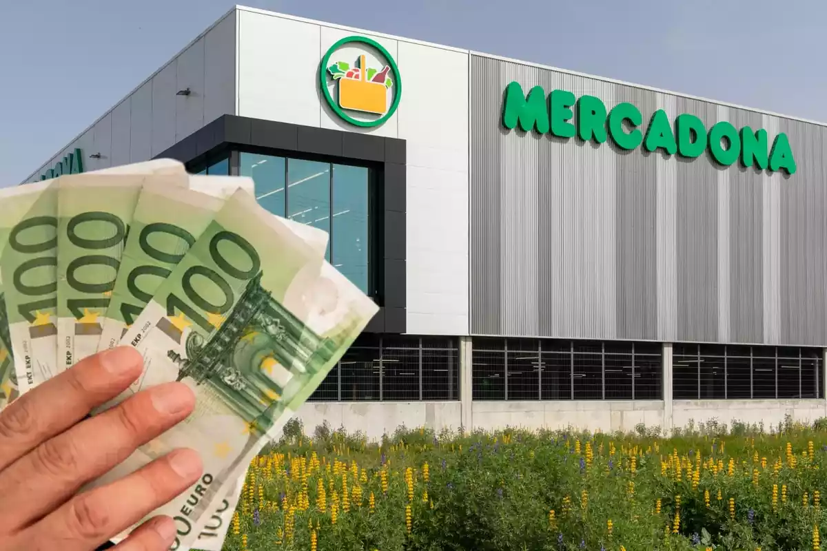Una mano sujeta billetes de cien euros delante de un supermercado de Mercadona