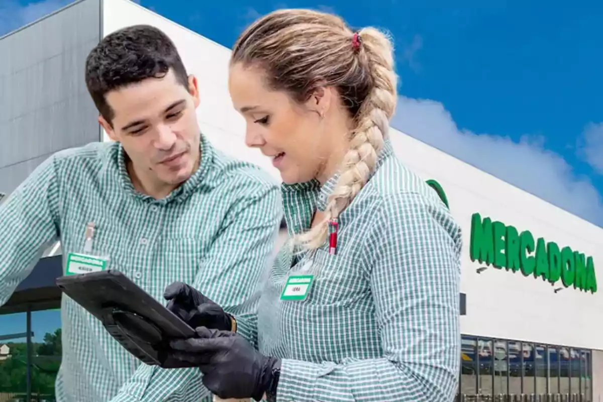 Dos empleados de Mercadona con uniforme verde revisan una tableta frente a la tienda.