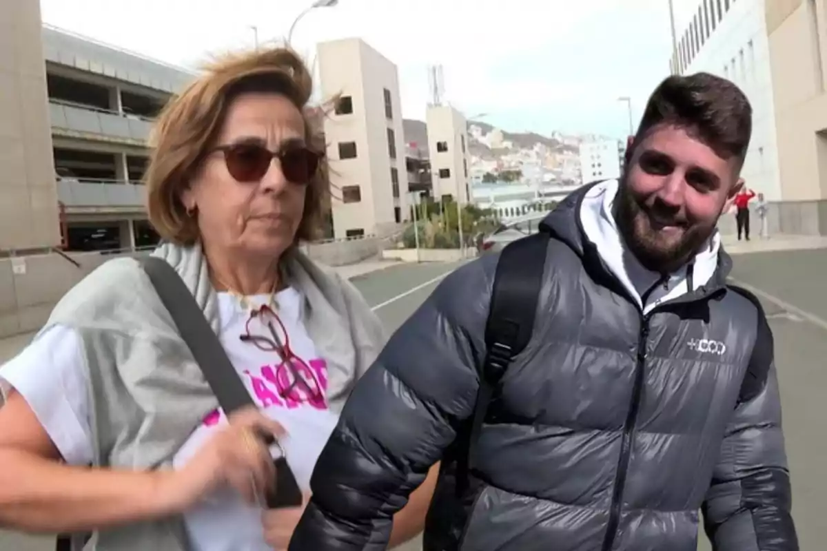 Dos personas caminando al aire libre con edificios de fondo.