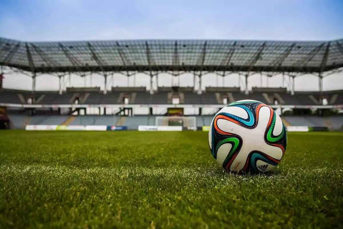 Balón de fútbol en el césped de un estadio vacío.