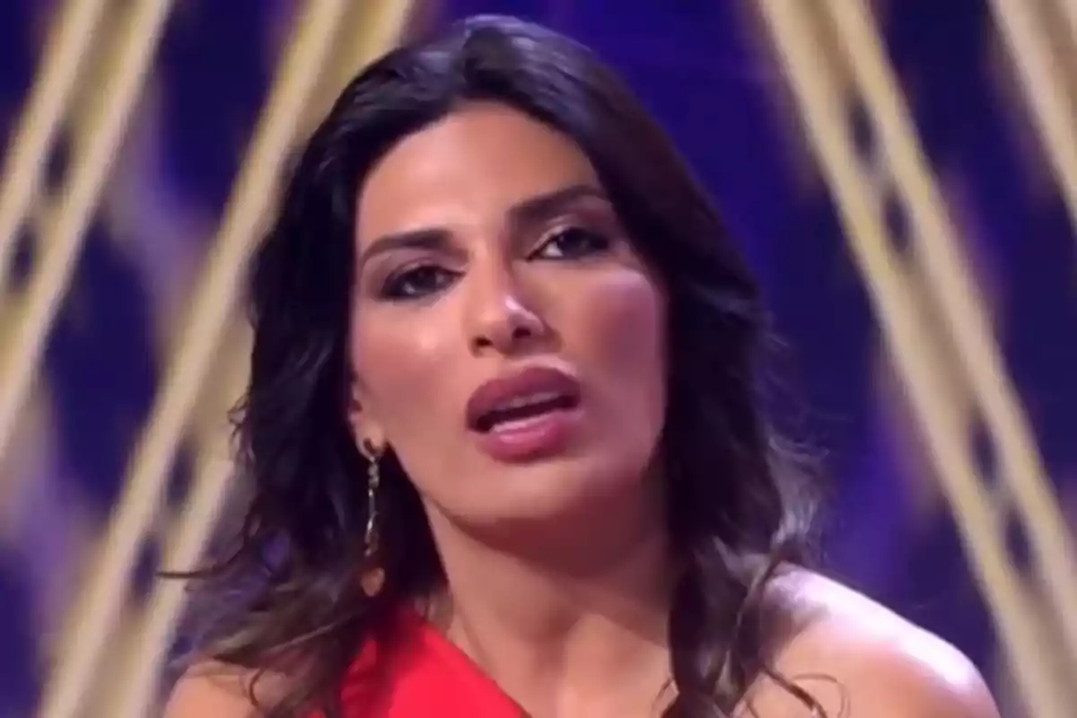Mujer con vestido rojo y cabello suelto en un escenario con fondo decorativo. Mujer con vestido rojo y cabello suelto en un escenario con fondo decorativo.