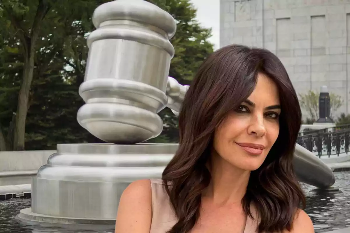 Una mujer de cabello oscuro posa frente a una escultura gigante de un mazo de juez en un entorno al aire libre.