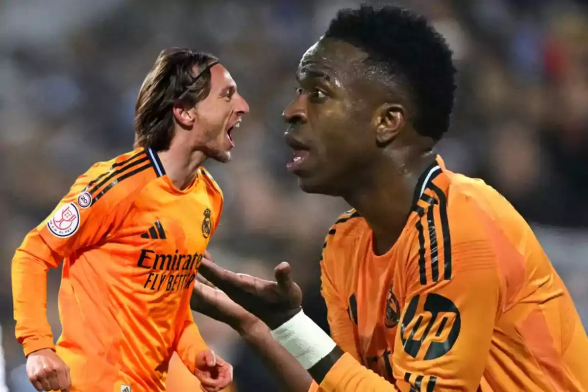 Dos jugadores de fútbol con uniforme naranja del Real Madrid en una expresión intensa durante un partido.