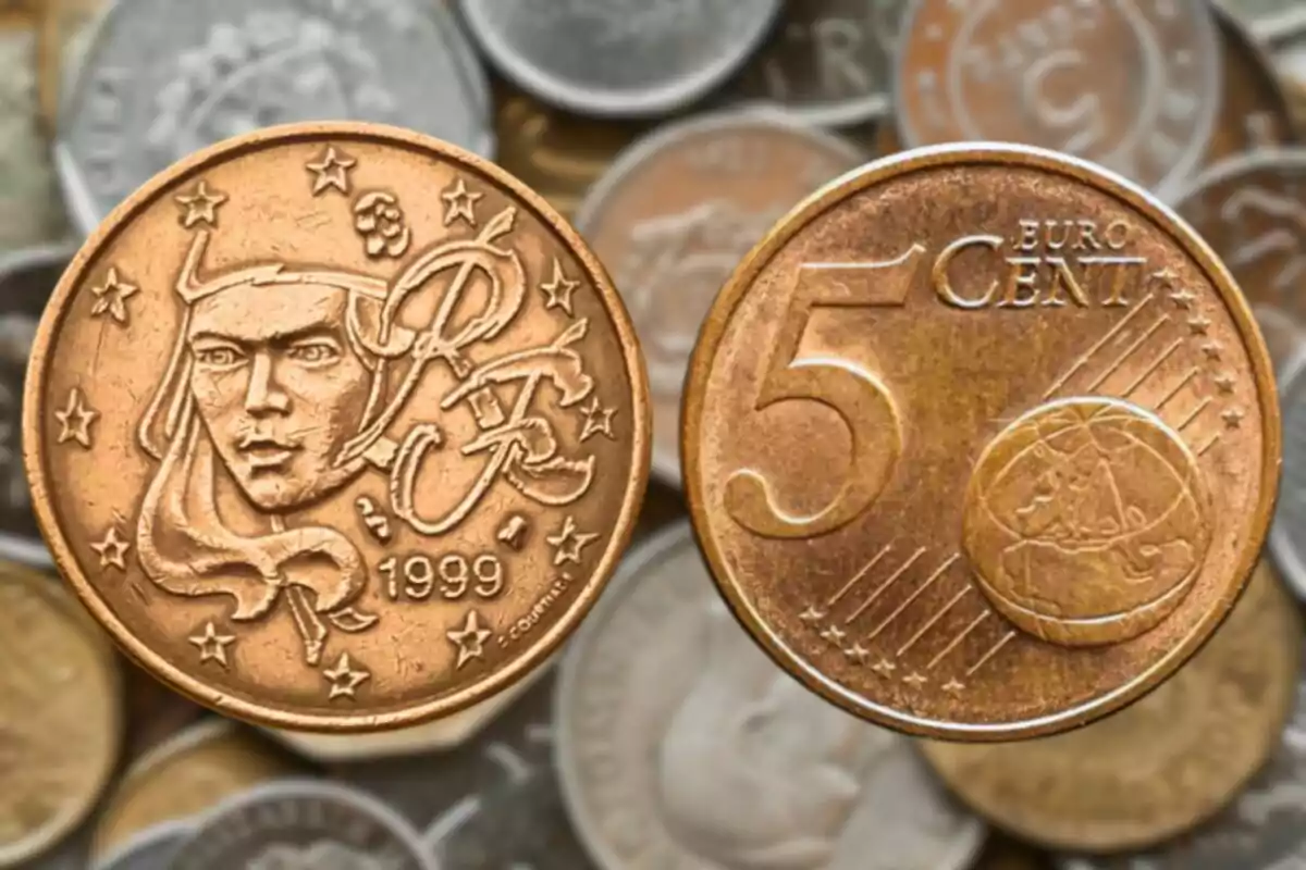 La imagen muestra dos monedas, una de 5 céntimos de euro y otra con un diseño que incluye una cara y el año 1999, ambas sobre un fondo de otras monedas desenfocadas.