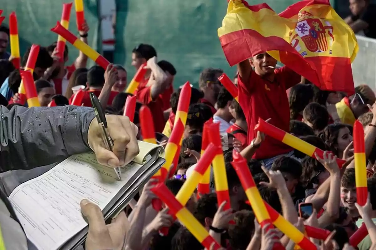 Una multitud de personas con camisetas rojas y amarillas y banderas de España celebran mientras una mano sostiene un bolígrafo y escribe en un cuaderno.