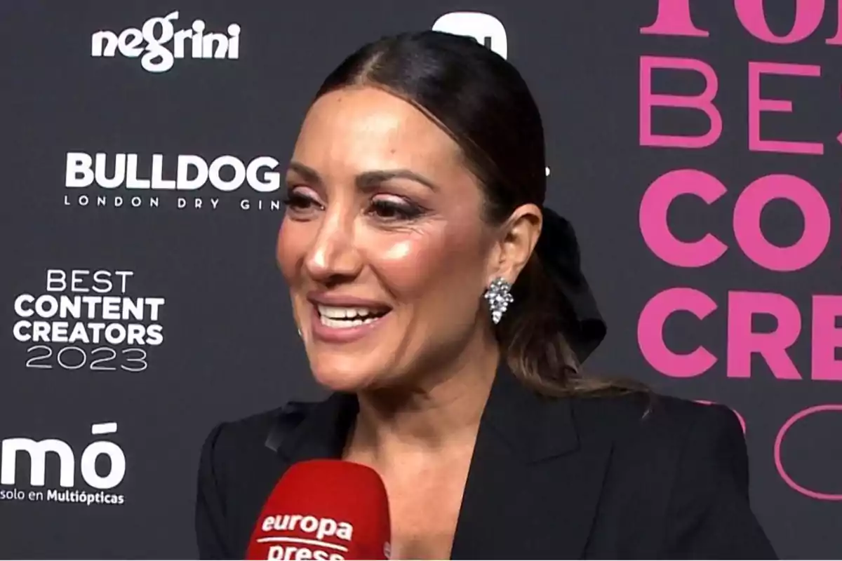 Una mujer sonriente con pendientes brillantes y cabello recogido, sosteniendo un micrófono de Una mujer sonriente con pendientes brillantes y cabello recogido, sosteniendo un micrófono de