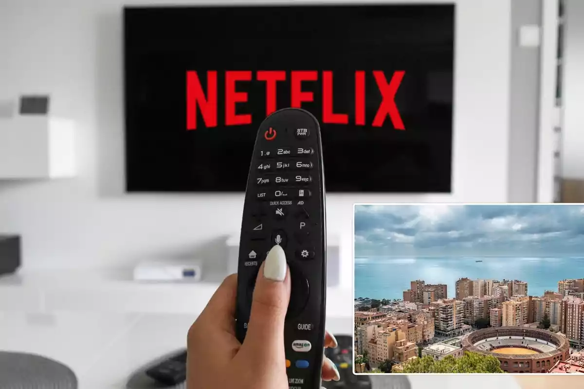 Una mano sosteniendo un control remoto frente a una pantalla de televisión con el logotipo de Netflix y una imagen insertada de una ciudad costera con edificios y una plaza de toros.