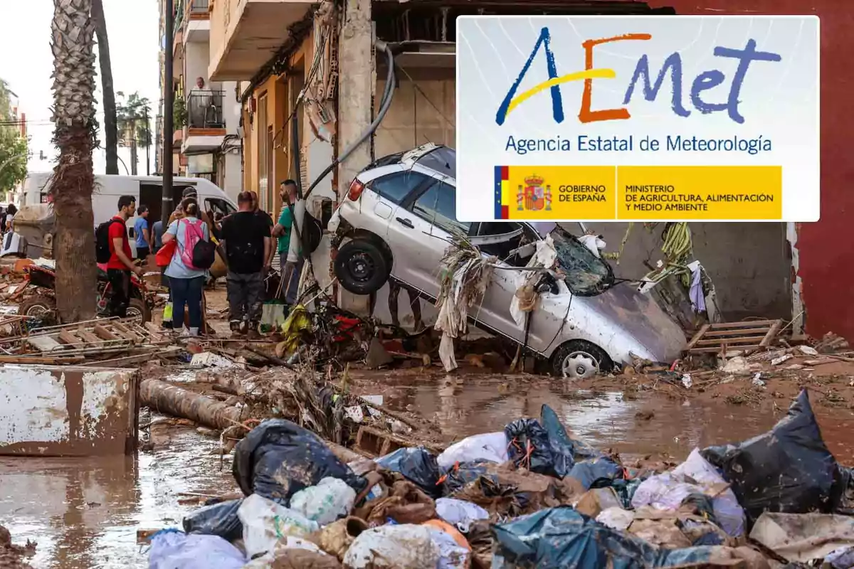 Personas observan los daños causados por una inundación en una calle llena de escombros y un coche volcado, con un cartel de la Agencia Estatal de Meteorología en la esquina superior derecha.