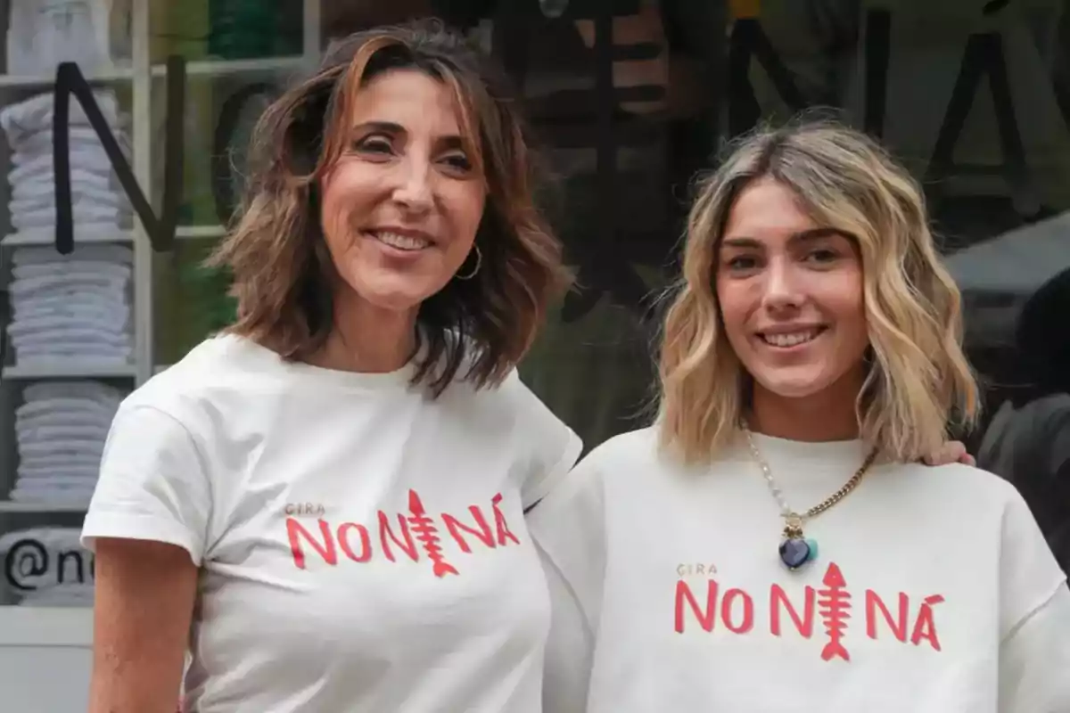 Dos mujeres sonrientes posan juntas usando camisetas blancas con el texto Gira No Ni Ná en letras rojas Dos mujeres sonrientes posan juntas usando camisetas blancas con el texto Gira No Ni Ná en letras rojas