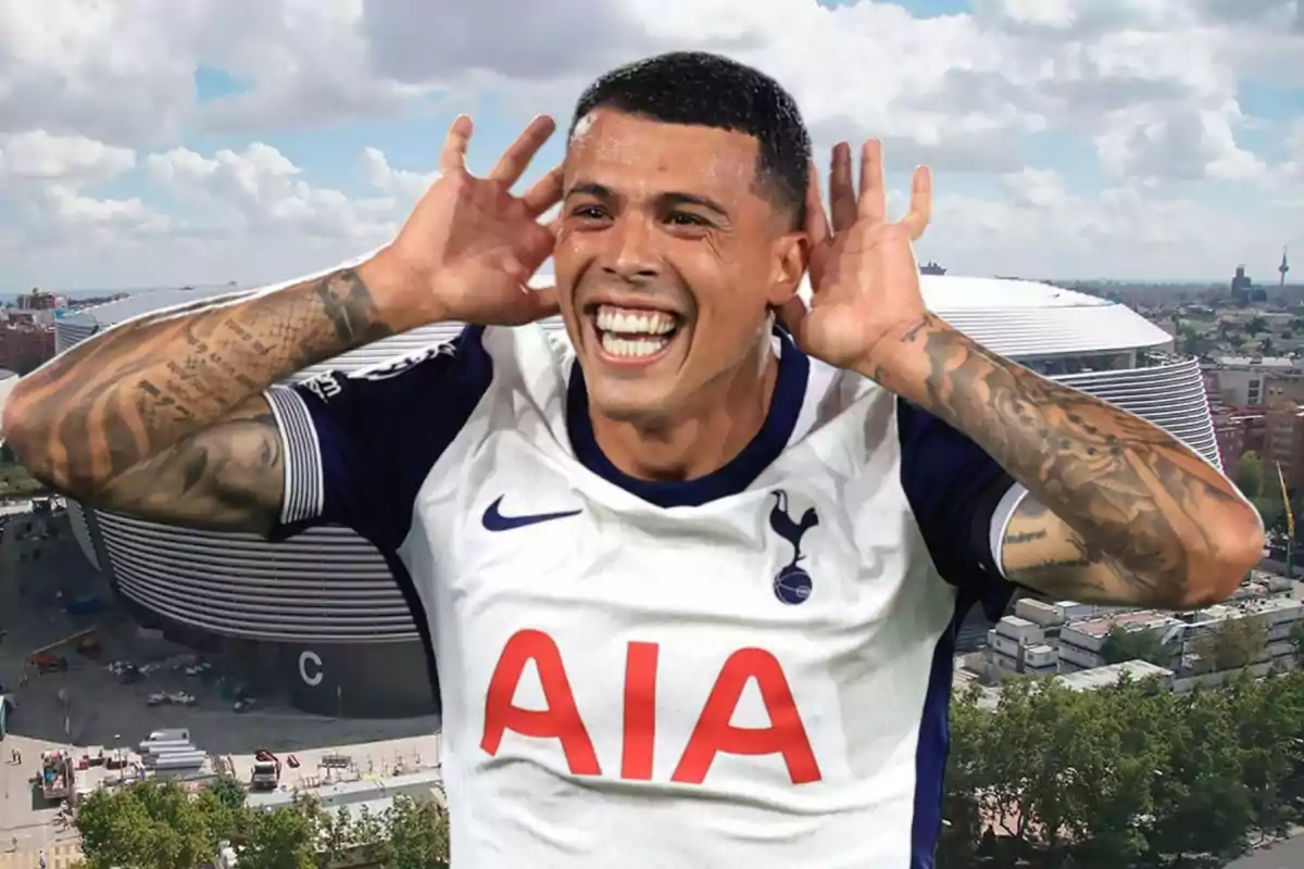 Un jugador de fútbol sonriente con la camiseta del Tottenham Hotspur celebrando con las manos en las orejas frente a un estadio moderno.