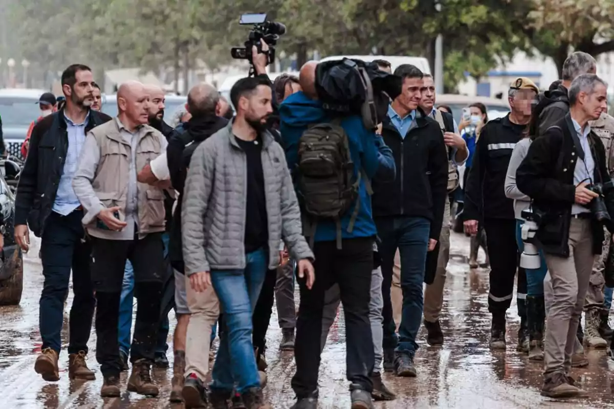 Un grupo de personas camina por una calle mojada mientras algunos llevan cámaras y equipos de grabación.