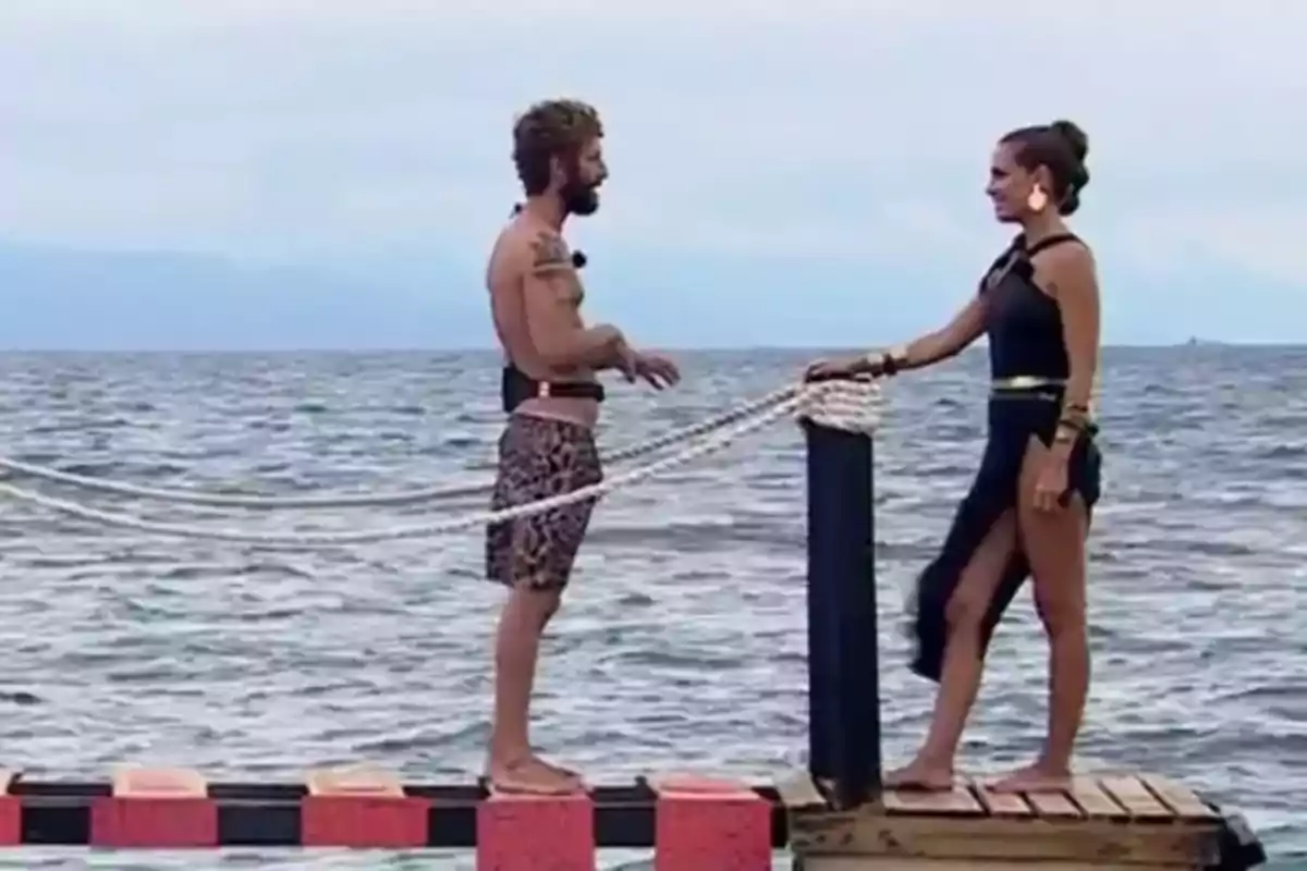 Dos personas de pie sobre una plataforma en el mar, una frente a la otra, con una cuerda entre ellas. Dos personas de pie sobre una plataforma en el mar, una frente a la otra, con una cuerda entre ellas.