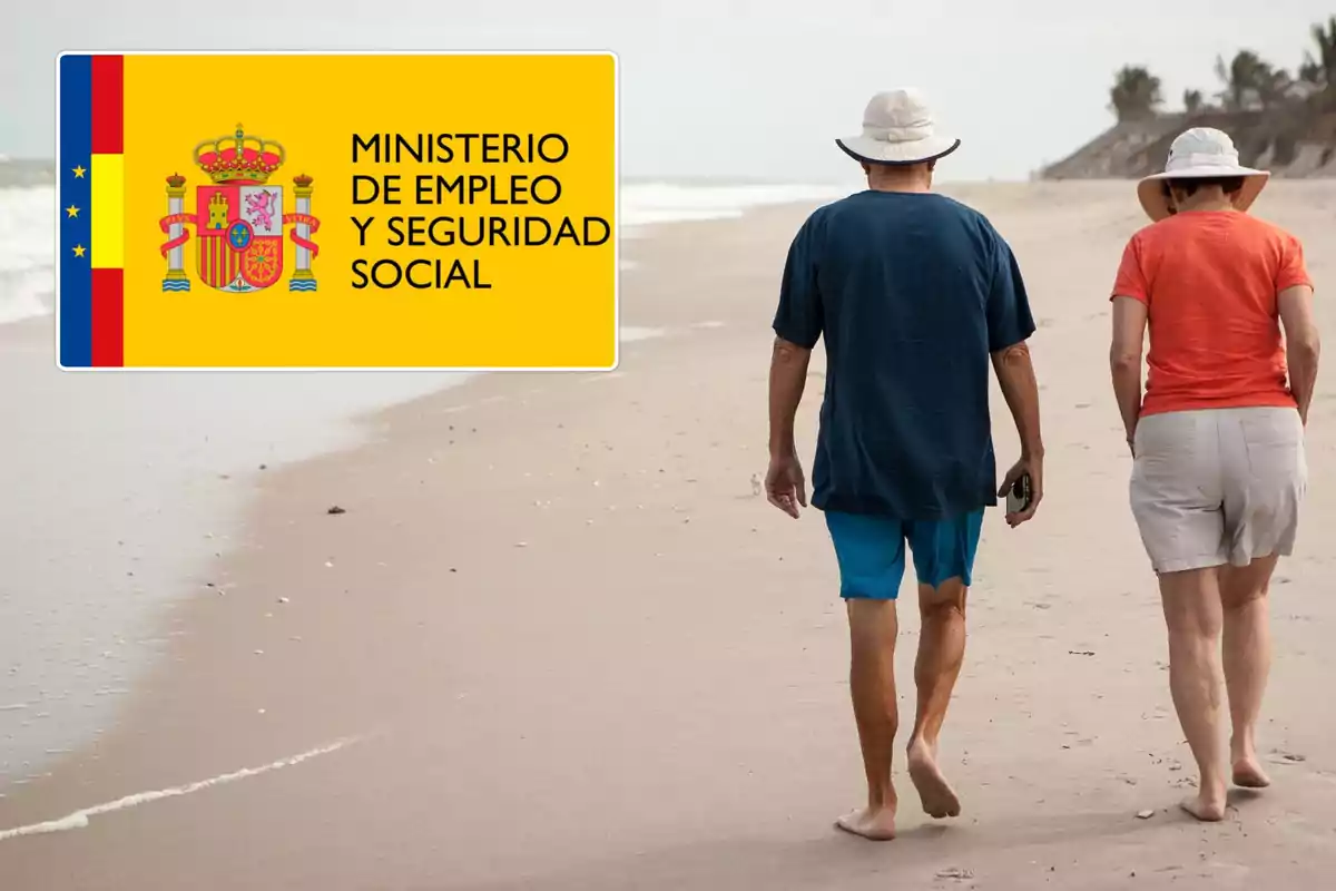 Una pareja de personas mayores caminando por la playa junto a un cartel del Ministerio de Empleo y Seguridad Social de España.