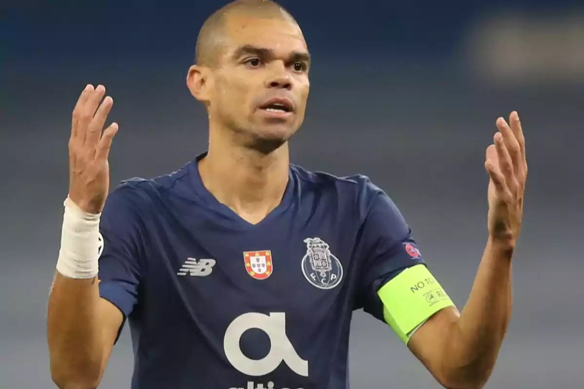 Jugador de fútbol con uniforme azul y brazalete de capitán verde levantando las manos.