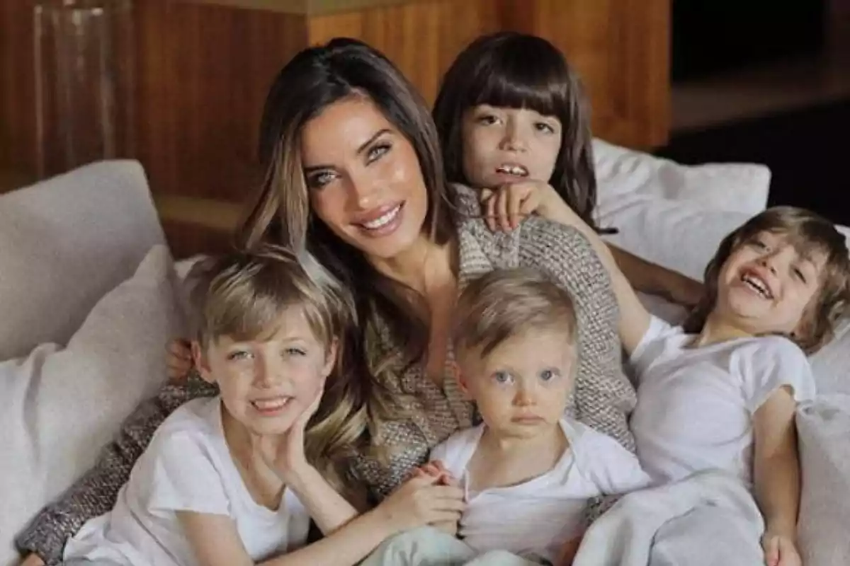 Una mujer sonriente rodeada de cuatro niños pequeños en un sofá. Una mujer sonriente rodeada de cuatro niños pequeños en un sofá.