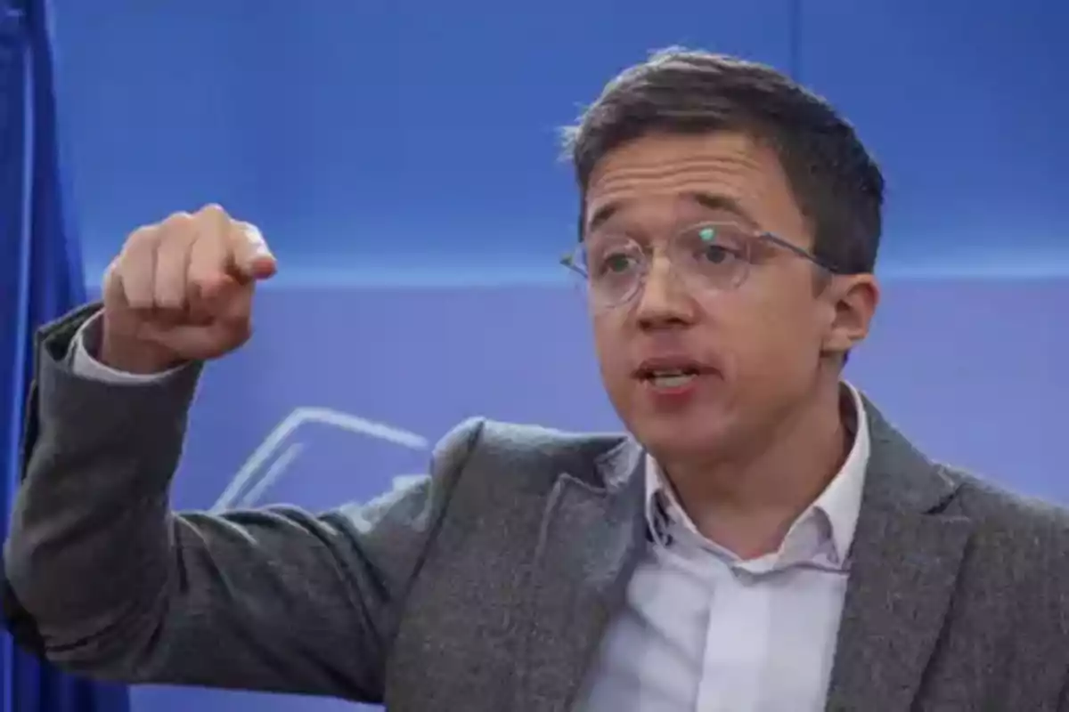 Un hombre con gafas y traje gesticula mientras habla frente a un fondo azul.