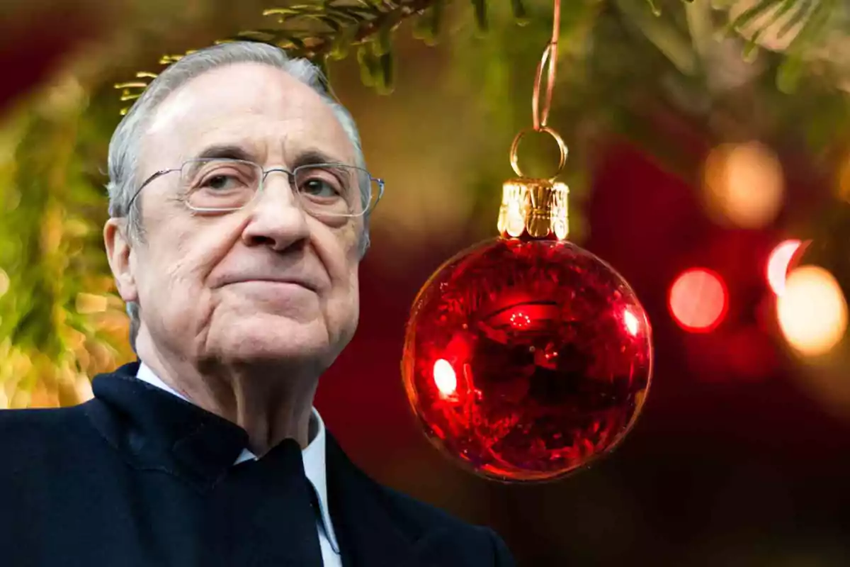 Un hombre mayor con gafas junto a un adorno navideño rojo colgando de un árbol.