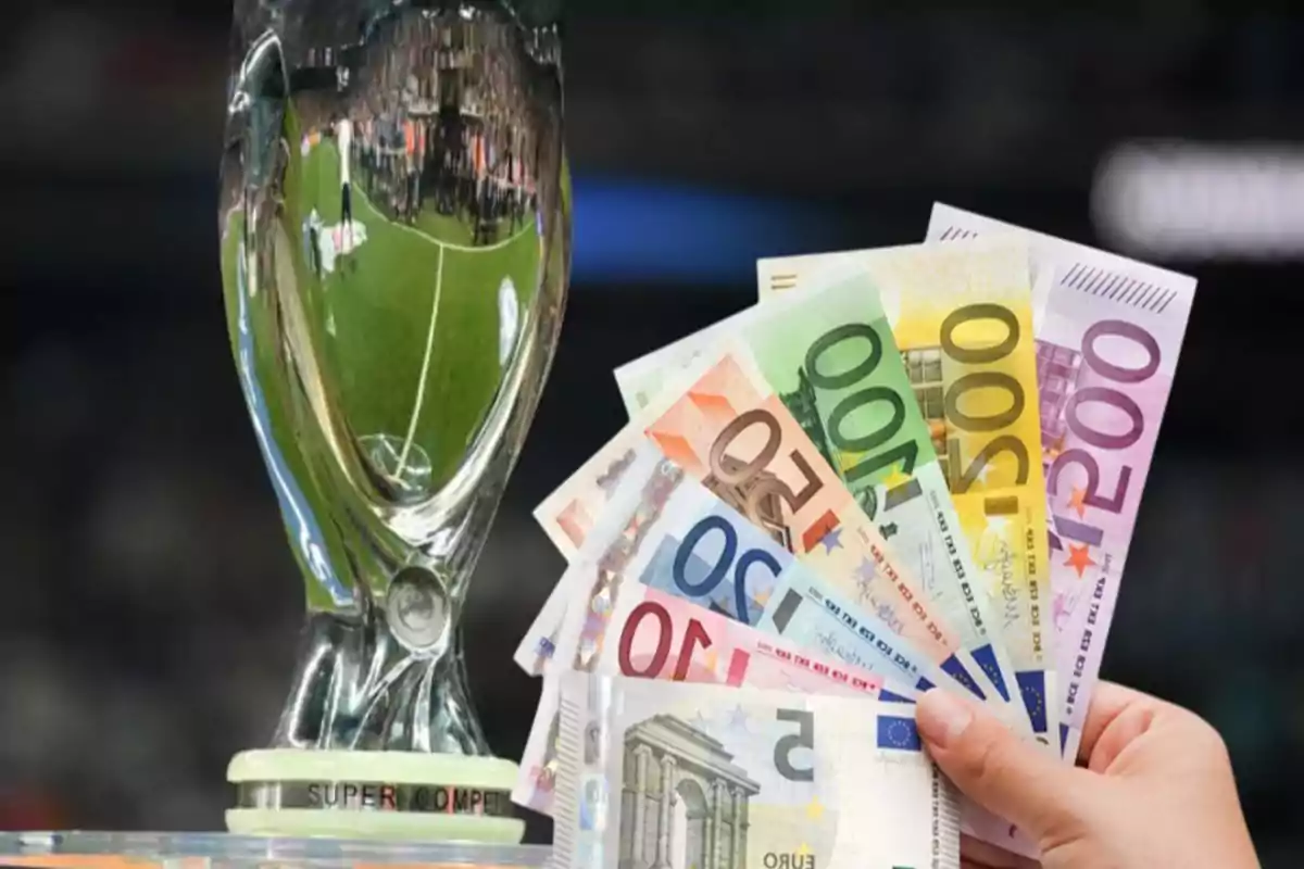 Una mano sosteniendo billetes de euro frente a un trofeo de fútbol.