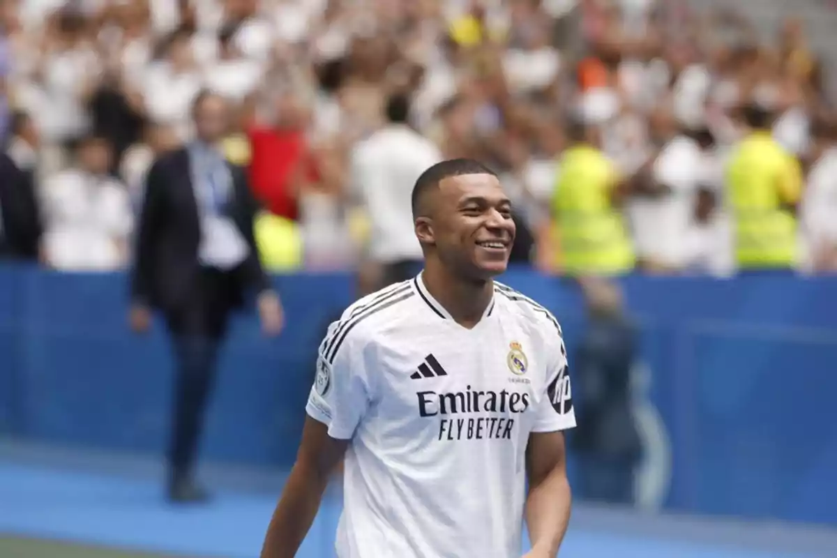 Un jugador de fútbol sonriente con la camiseta del Real Madrid en un estadio lleno de aficionados.