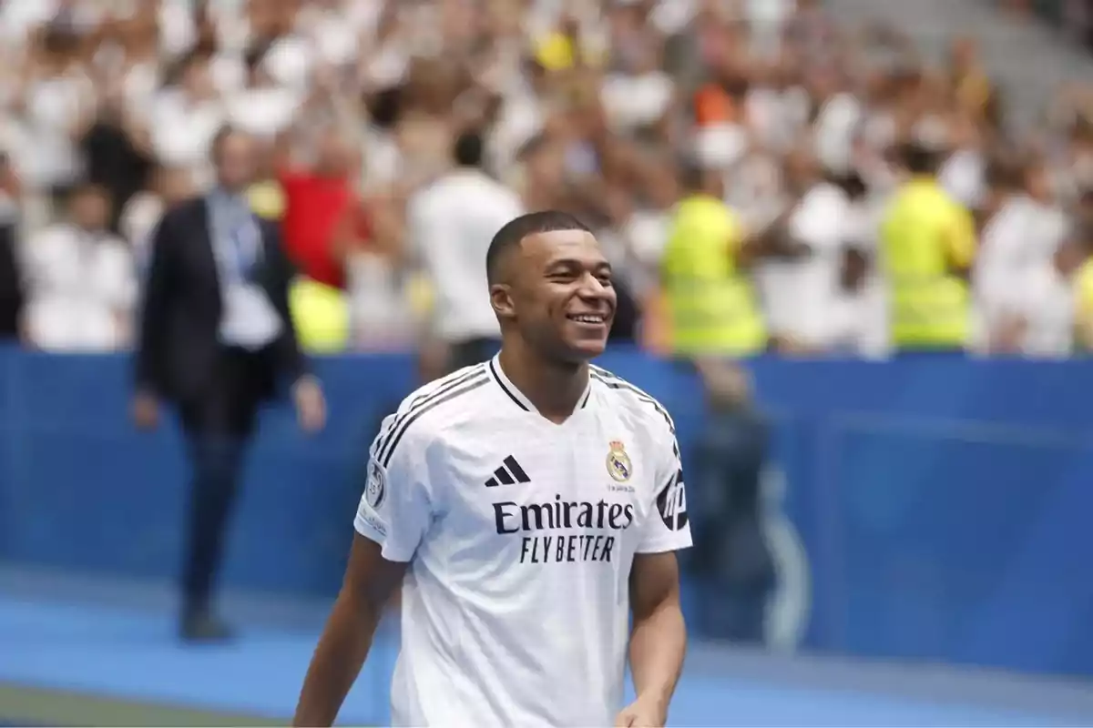 Un jugador de fútbol sonríe mientras viste la camiseta del Real Madrid en un estadio lleno de espectadores.